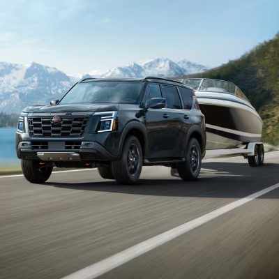 All-new 2025 Nissan Armada towing a boat on a scenic mountain road.