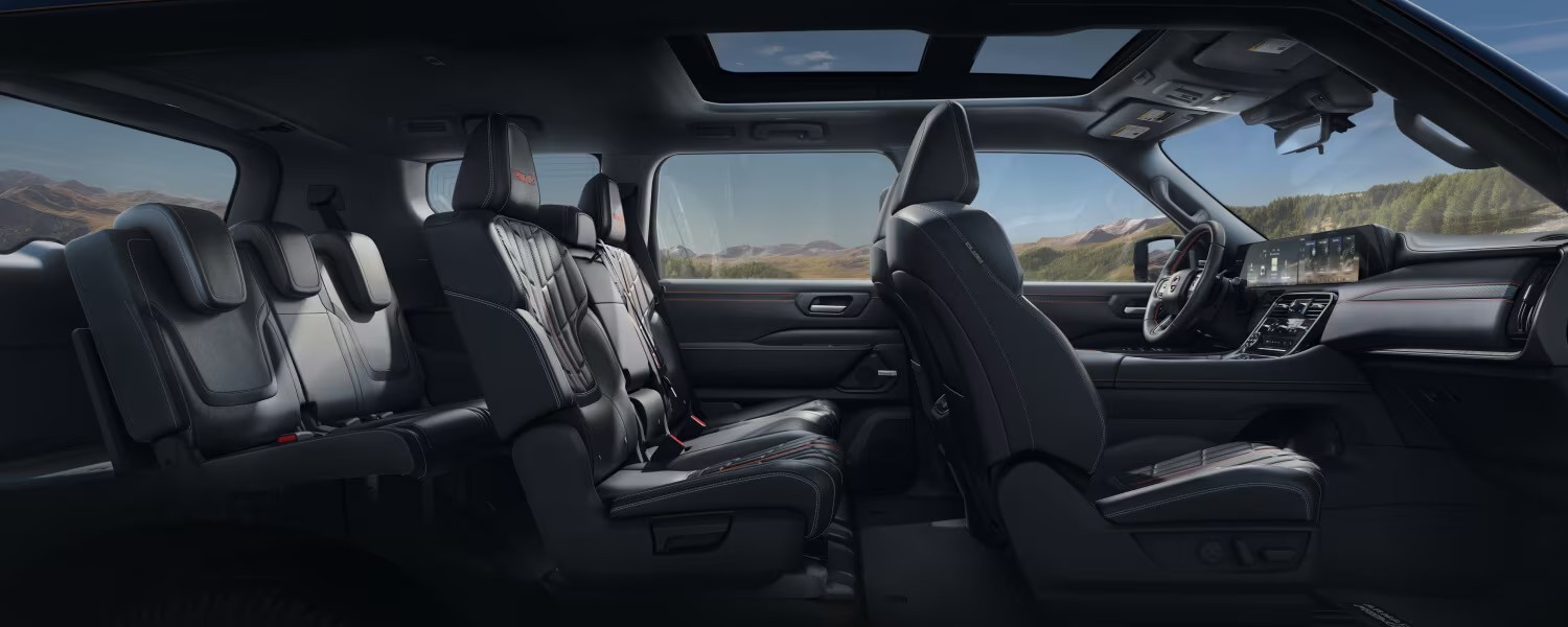 Interior view of the 2025 Nissan Armada showcasing its spacious three-row seating, premium black leather upholstery with red accents, and panoramic windows offering scenic outdoor views