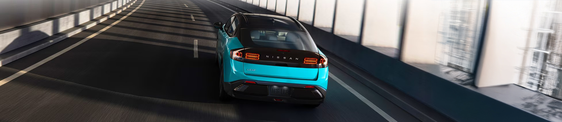 2026 Nissan Leaf in blue driving up a curved ramp in a parking structure with filtered sun shining in on side width=